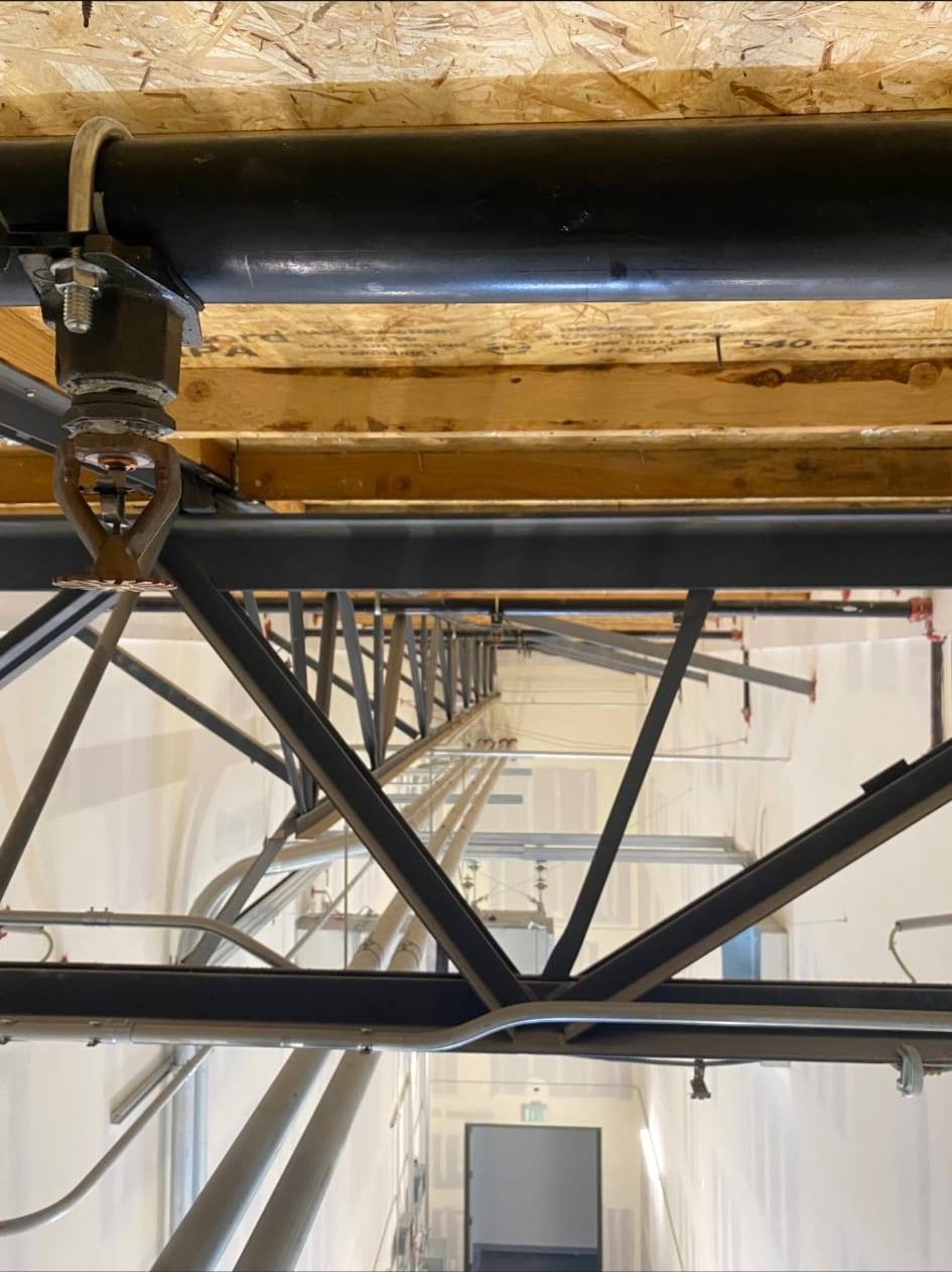 Pendent fire sprinkler head and branch piping with bracing beneath a wood-framed floor deck in a residential building corridor